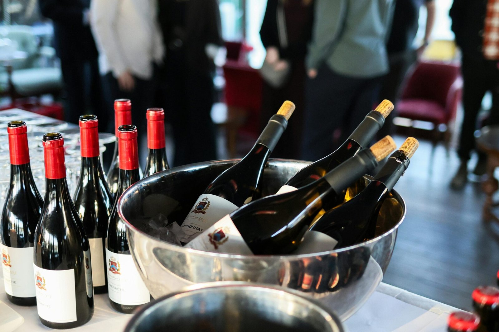 Upscale gathering with wine bottles and people mingling indoors, creating a sophisticated ambiance.